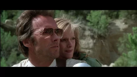 HD PC desktop wallpaper — movie still from The Gauntlet: close-up of a man in aviator sunglasses holding a concerned woman, sunlit canyon cliffs in the background.