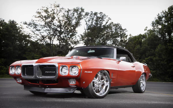 HD PC desktop wallpaper featuring a classic red Pontiac Firebird parked on pavement with trees in the background.