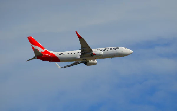 A Qantas Boeing 737 soaring through a clear sky, showcasing its distinctive red and white livery, set against a serene backdrop—an engaging HD desktop wallpaper for aviation enthusiasts.