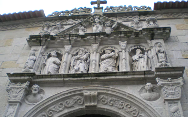 HD wallpaper depicting ornate religious Christian stone carvings and sculptures on a church facade, with intricate details and a cross at the top.