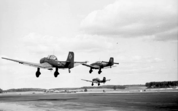 Black and white HD desktop wallpaper showing three Junkers Ju 87 military aircraft flying low over a runway under a cloudy sky.
