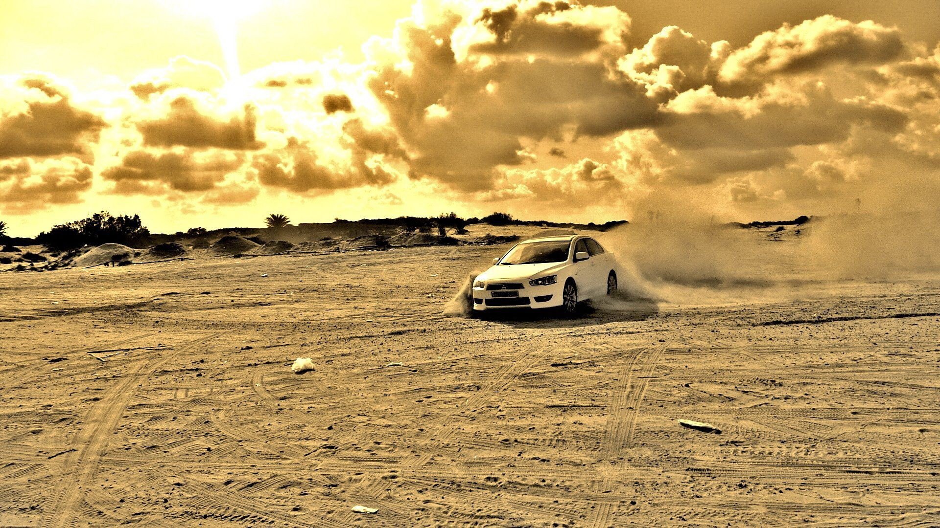 HD PC desktop wallpaper background: Mitsubishi Motors vehicle drifting across sandy terrain, kicking up dust under dramatic golden clouds.