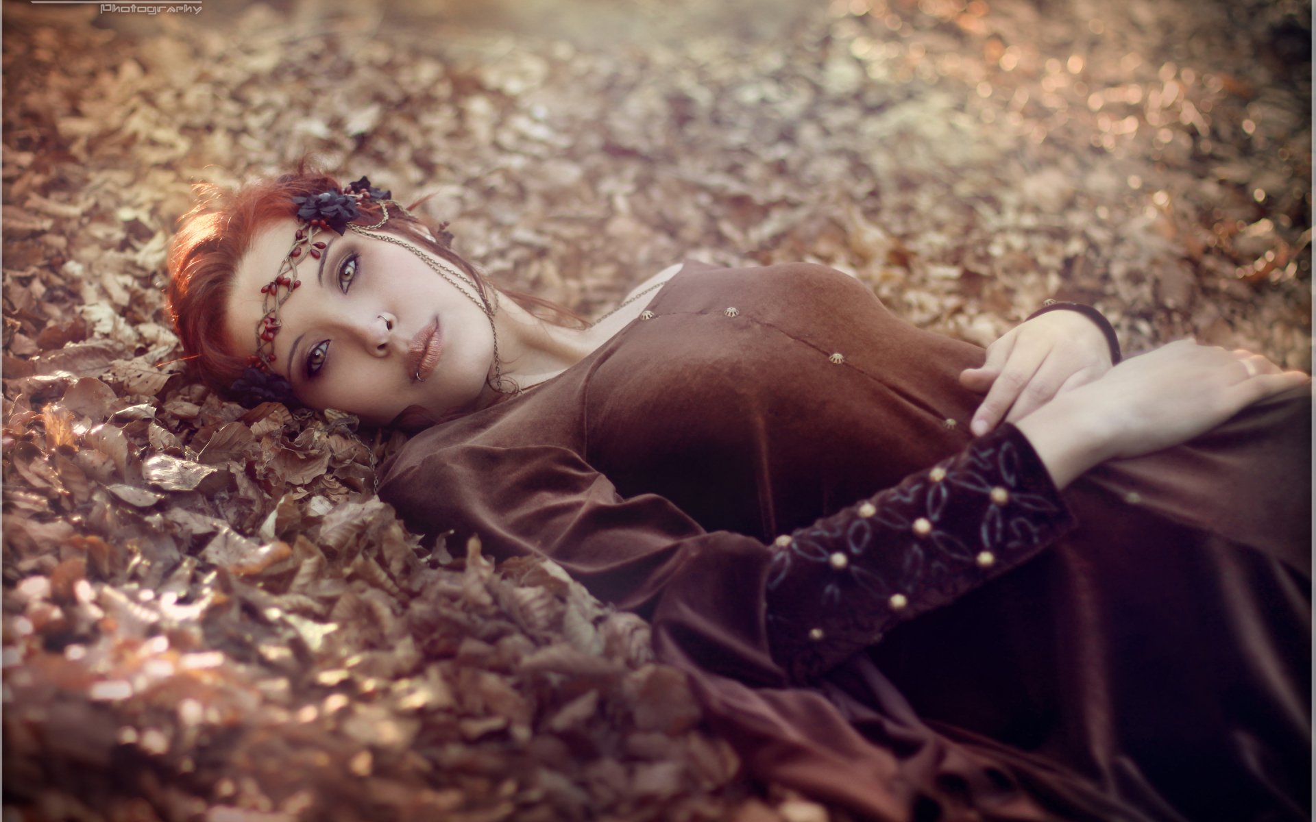 A serene woman lies amidst autumn leaves, adorned with a delicate floral accessory, exuding a tranquil mood. This HD image makes a stunning desktop wallpaper and background.