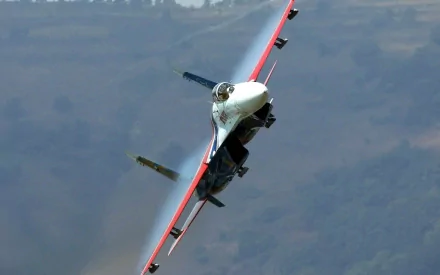 HD desktop wallpaper featuring a military jet performing a low, sharp turn during an air show against a blurred mountainous background.