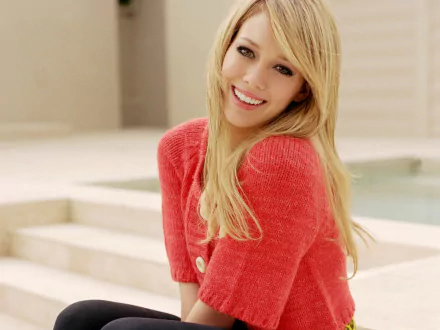 HD PC desktop wallpaper featuring celebrity Hilary Duff smiling in a coral sweater with a blurred outdoor background.