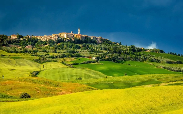 HD desktop wallpaper of Pienza, a man-made hilltop town in Tuscany, Italy, surrounded by vibrant green and yellow fields under a clear blue sky.