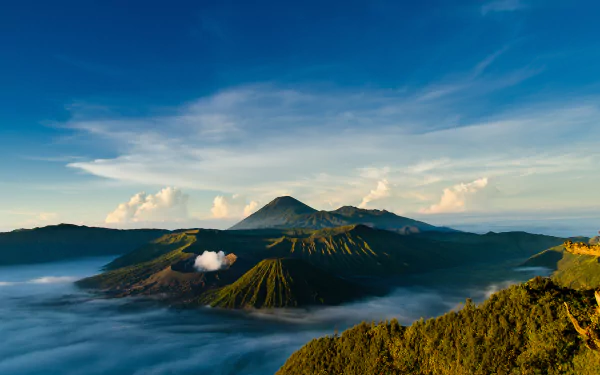 HD desktop wallpaper of Indonesia’s volcanic landscape with misty hills under a vibrant blue sky, showcasing nature’s dramatic beauty.