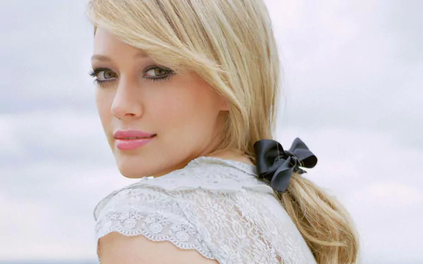 A serene portrait of Hilary Duff, showcasing her blonde hair tied with a black bow, set against a soft, cloudy background. This image serves as an HD desktop wallpaper.