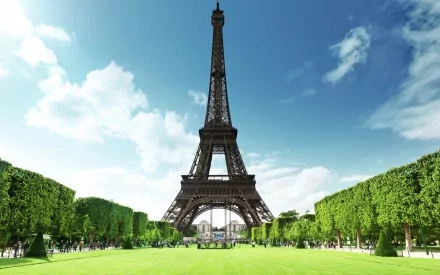 HD desktop wallpaper of the Eiffel Tower in Paris, centered against a bright sky, surrounded by lush green lawns and trees.
