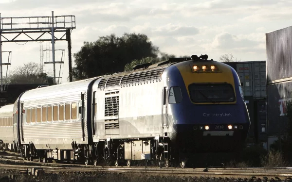 HD PC desktop wallpaper/background: New South Wales XPT train vehicle racing along sunlit tracks under a cloudy sky with rail gantries.
