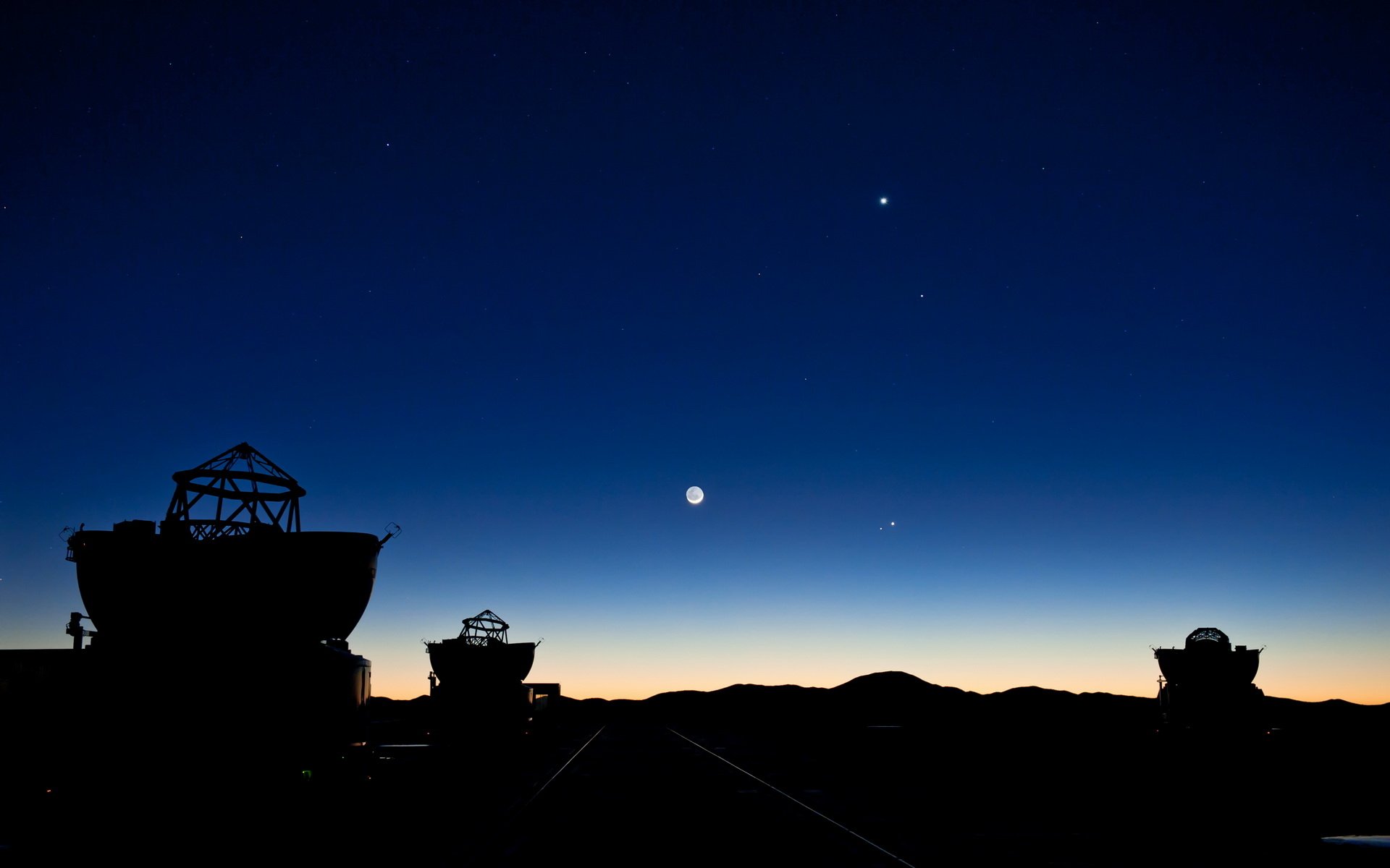 HD PC desktop wallpaper of silhouetted man-made telescopes at twilight, with bright planets and stars above a dark horizon.