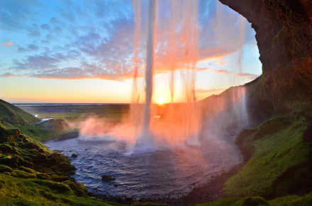 HD wallpaper of Seljalandsfoss waterfall in Iceland, capturing a stunning sunrise or sunset filtering through the cascading water.