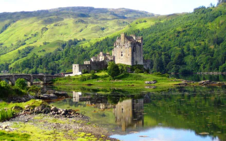 Eilean Donan Castle sits majestically on a lush green island, surrounded by serene waters, reflecting the stunning Scottish landscape in this HD desktop wallpaper.