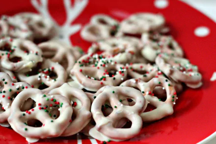 HD desktop wallpaper featuring white chocolate-covered pretzels sprinkled with red and green holiday-themed decorations on a red plate.