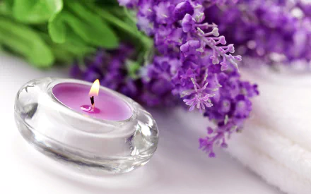 HD wallpaper featuring a lit purple candle in a clear holder, accompanied by fresh lavender flowers and white towels, evoking a serene ambiance.