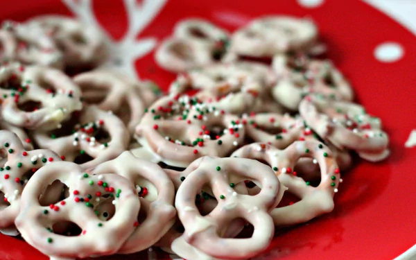 HD desktop wallpaper featuring white chocolate-covered pretzels sprinkled with red and green holiday-themed decorations on a red plate.