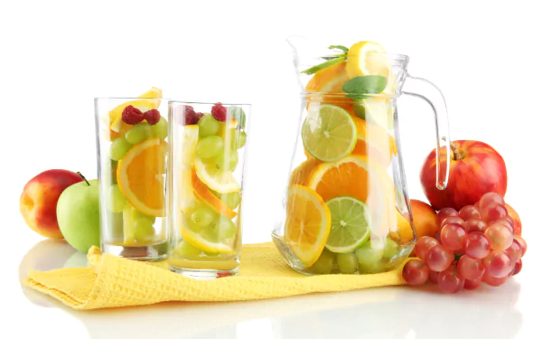 A vibrant collection of fresh fruit, including apples, grapes, and citrus, is arranged with glasses and a pitcher of infused water on a yellow cloth. This HD desktop wallpaper celebrates refreshing food.