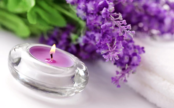 HD wallpaper featuring a lit purple candle in a clear holder, accompanied by fresh lavender flowers and white towels, evoking a serene ambiance.