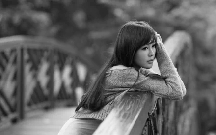 HD desktop wallpaper featuring a monochrome image of an Asian woman leaning thoughtfully on a bridge railing in a tranquil outdoor setting.