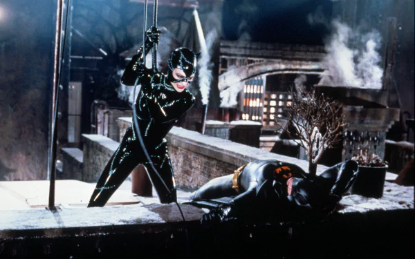 Batman Returns 2K Quad HD PC desktop wallpaper: Catwoman in glossy black suit on a snowy rooftop, poised over a fallen Batman as gothic city smoke and lights glow behind them.