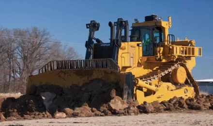 HD desktop wallpaper featuring a yellow Caterpillar D11 bulldozer pushing earth on a clear day with a blue sky and bare trees in the background.