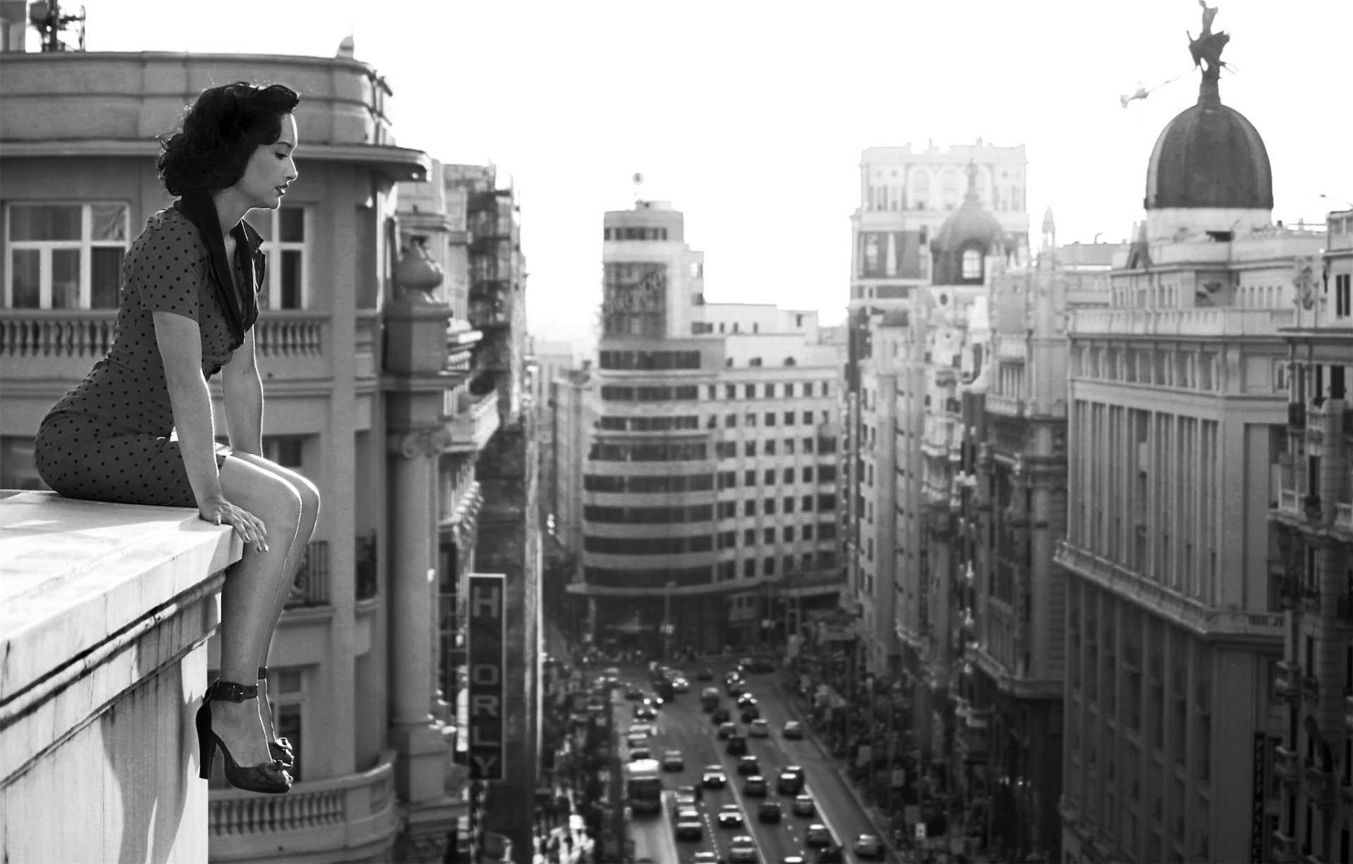 Black and white HD desktop wallpaper featuring a woman sitting on a high ledge overlooking a bustling city street.