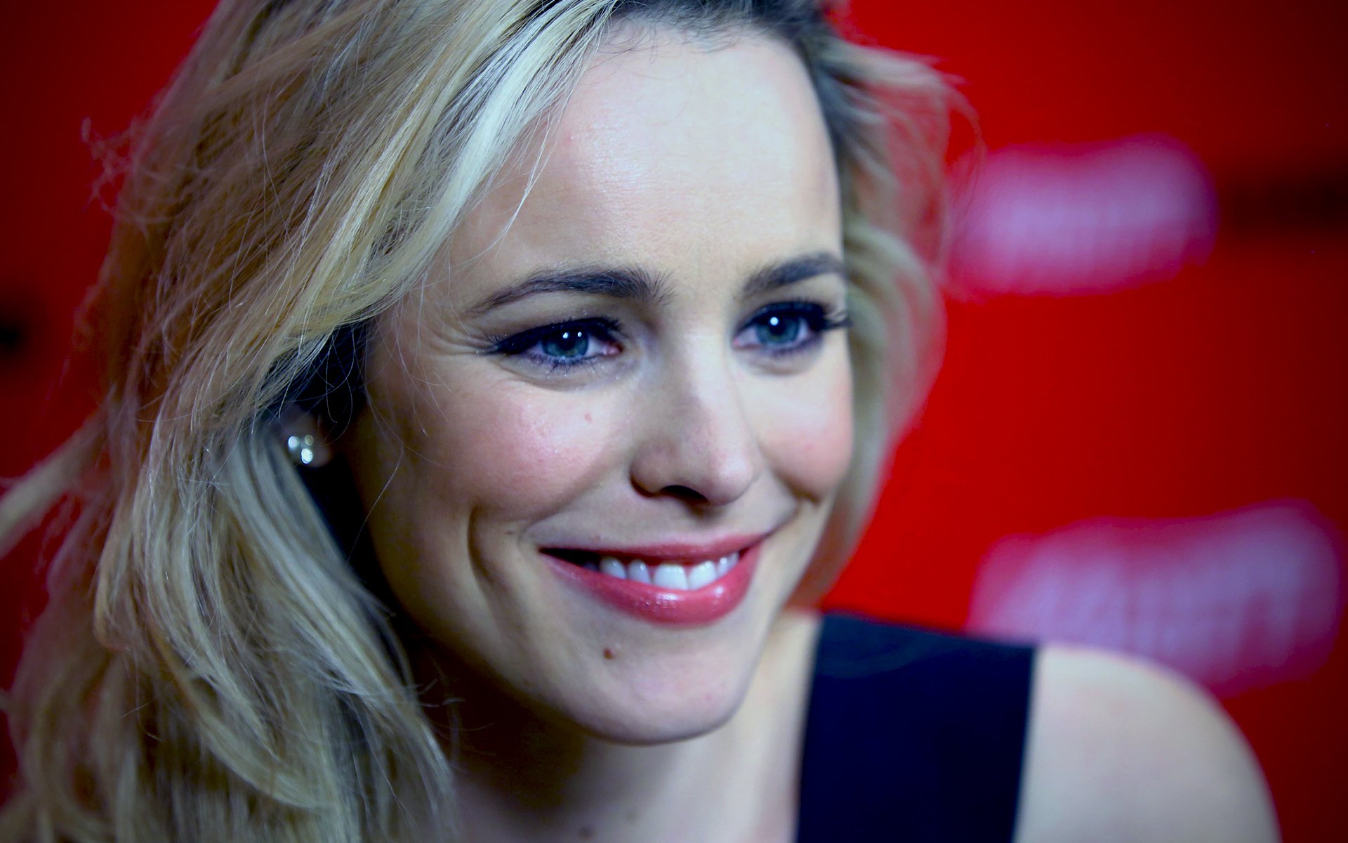 HD desktop wallpaper featuring a close-up of celebrity Rachel McAdams smiling against a blurred red background.
