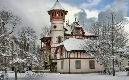 HD desktop wallpaper of a man-made villa covered in snow, surrounded by bare trees under a cloudy sky.