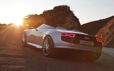 HD PC desktop wallpaper: white Audi vehicle parked on a coastal road at sunset, rear three-quarter view with illuminated taillights and rocky cliffs in the background.