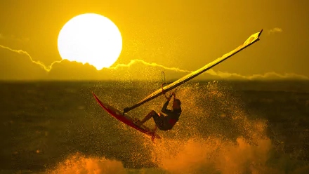 A windsurfer performs an impressive jump against a stunning sunset backdrop, capturing the thrill of the sport. This vibrant image serves as an inspiring HD desktop wallpaper.