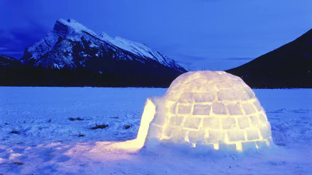 HD desktop wallpaper showing a glowing man-made igloo on a snowy landscape with a mountain under a deep blue sky.