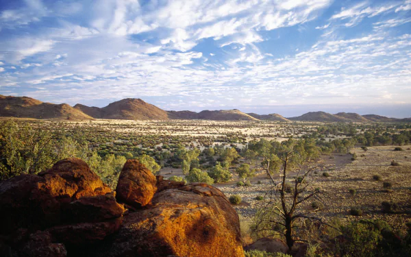 2K Quad HD PC desktop wallpaper: panoramic nature view of the Flinders Ranges — rocky foreground, scattered trees and distant ridges beneath a cloud-streaked sky.