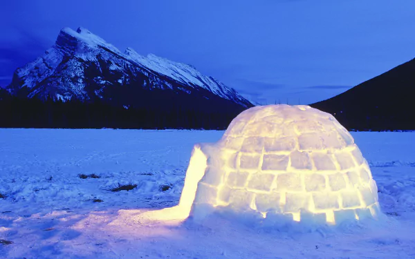 HD desktop wallpaper showing a glowing man-made igloo on a snowy landscape with a mountain under a deep blue sky.