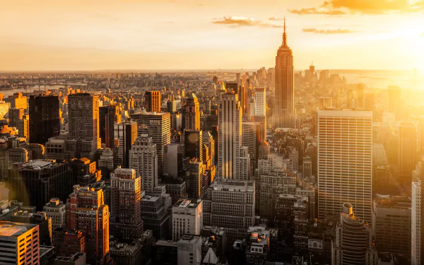 HD desktop wallpaper showcasing a sunlit New York City skyline with iconic man-made skyscrapers, including the Empire State Building, bathed in golden light.