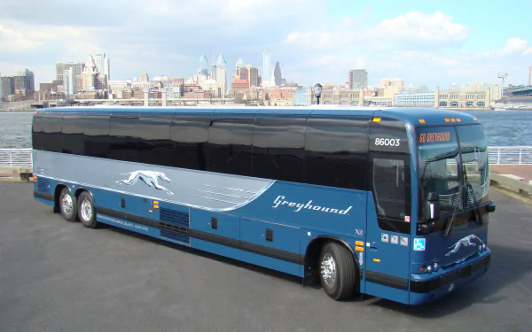 HD desktop wallpaper of a blue Greyhound bus parked by the waterfront with a city skyline in the background.