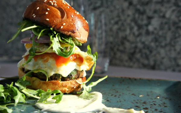 HD desktop wallpaper featuring a close-up of a juicy burger with fresh greens, melted cheese, and sauce on a sesame bun against a textured background.