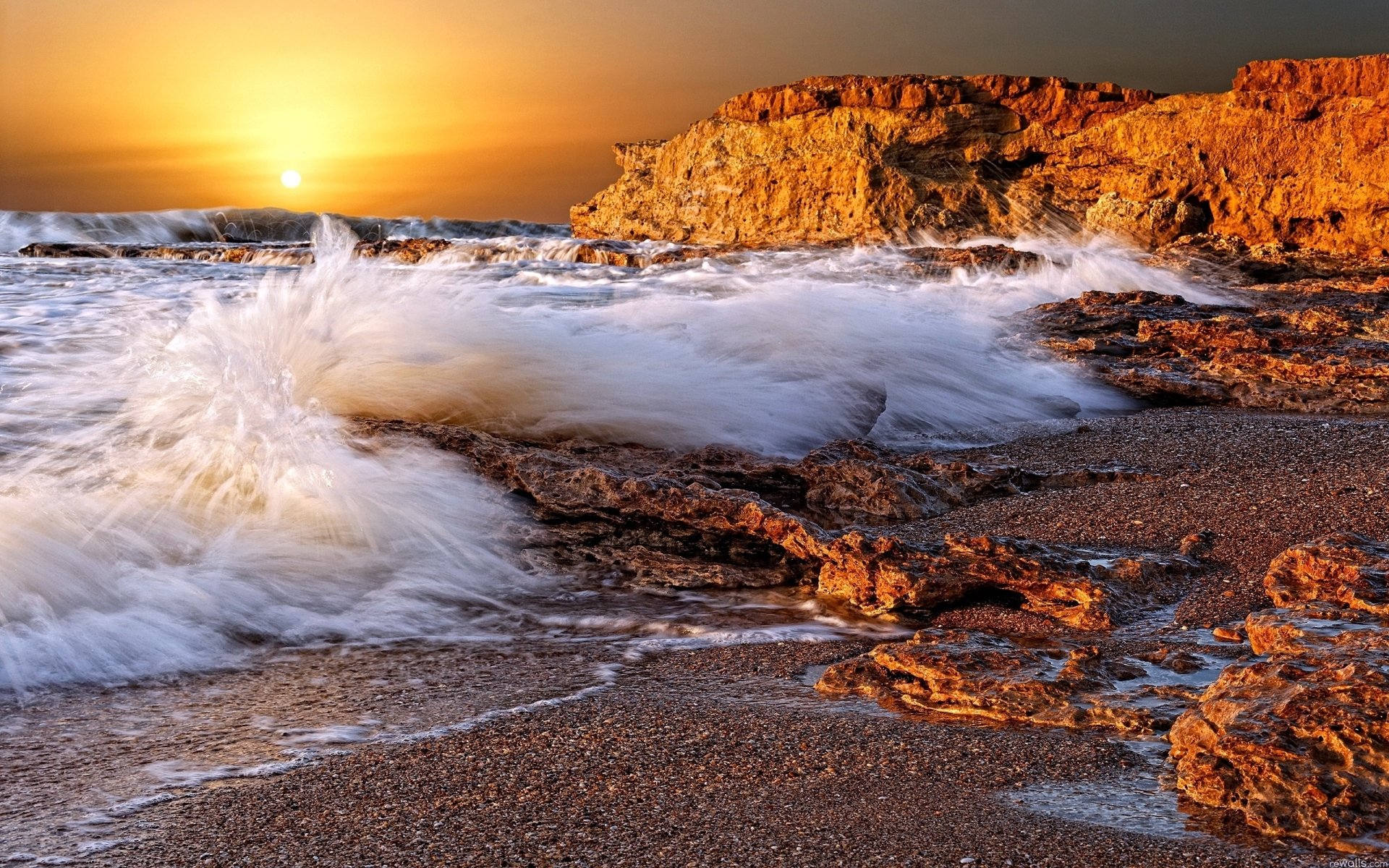 A stunning HD wallpaper featuring a serene coastline at sunset, with waves crashing against rocky shorelines, capturing the beauty of nature in vibrant colors.