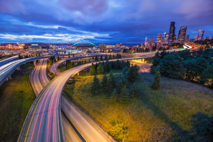 A vibrant Seattle cityscape at dusk with illuminated highways curving through green spaces, captured in high-definition for a dynamic desktop wallpaper.