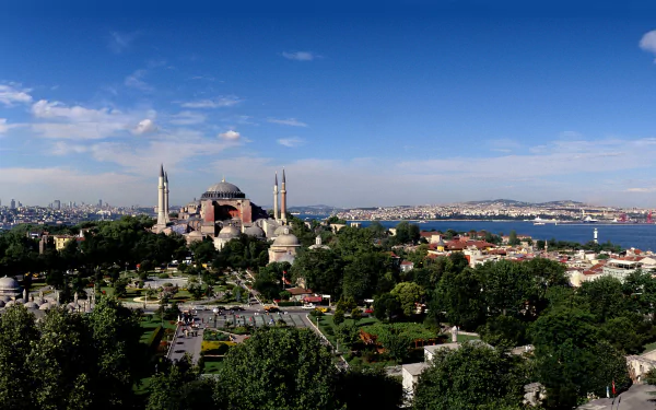 A breathtaking HD wallpaper featuring Hagia Sophia, surrounded by lush greenery and a vibrant cityscape, under a clear blue sky, embodying its rich religious and historical significance.