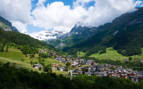 A stunning view of a Swiss village nestled in the mountains, showcasing lush greenery, snow-capped peaks, and a picturesque lake, capturing the natural beauty of Montreux and its surroundings.