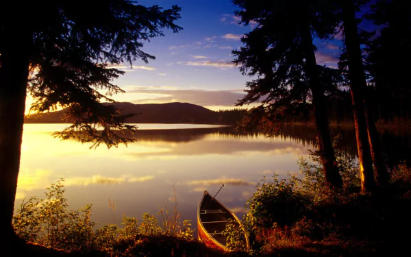 HD wallpaper of a serene lake at sunset, framed by silhouetted trees, with a canoe resting by the shore.