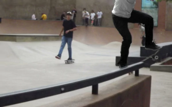 A dynamic 4K Ultra HD desktop wallpaper showing a skateboarder performing a grind trick on a rail in an indoor skatepark with other skaters in the background.