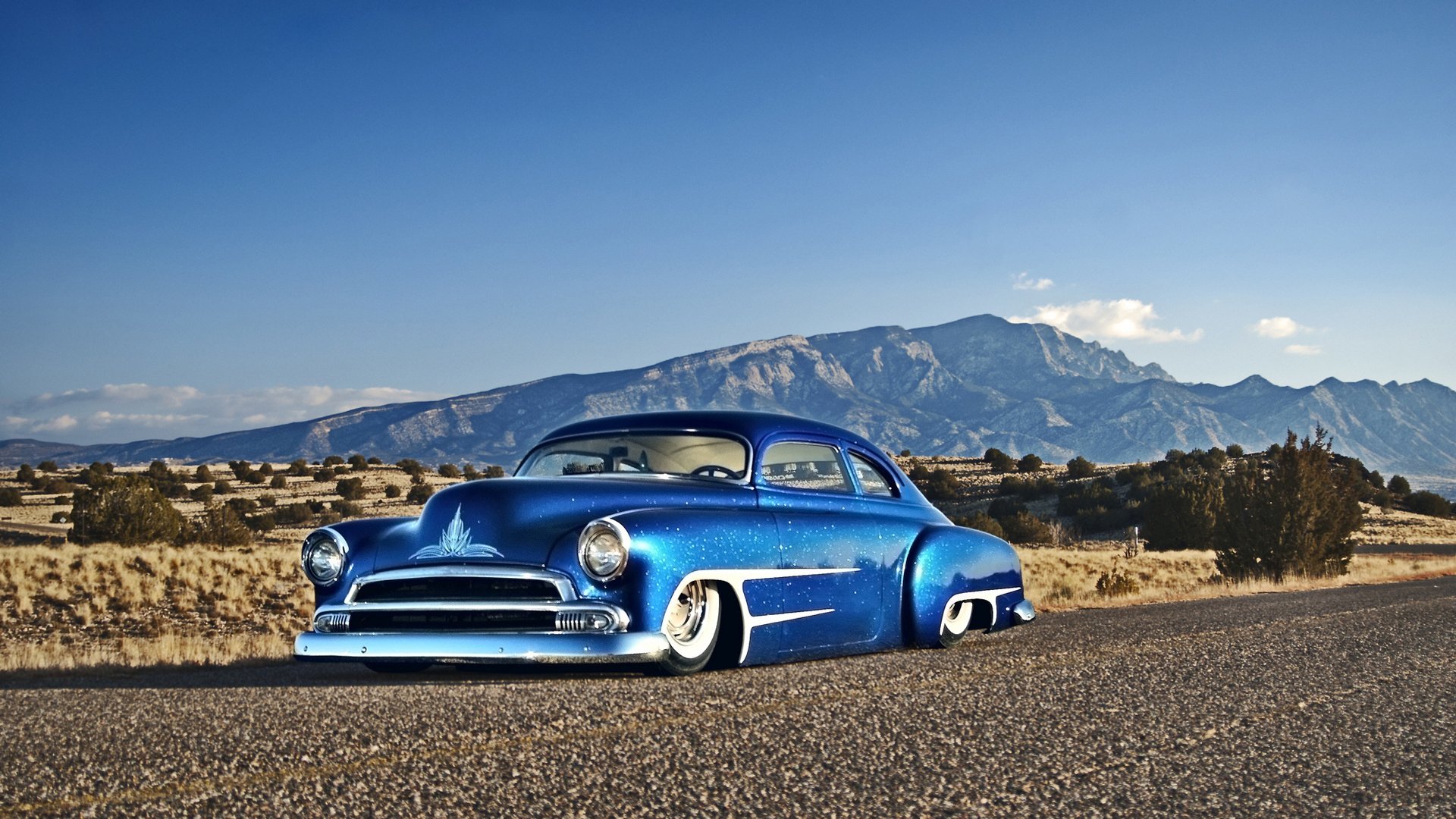 Blue 1951 Kaiser Dragon Coupe low to the ground on a desert road with mountains and clear sky — HD PC desktop wallpaper and background.