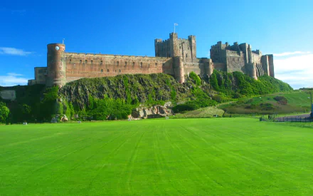 HD desktop wallpaper featuring Bamburgh Castle, a historic man-made fortress set against a clear blue sky and vibrant green lawn.