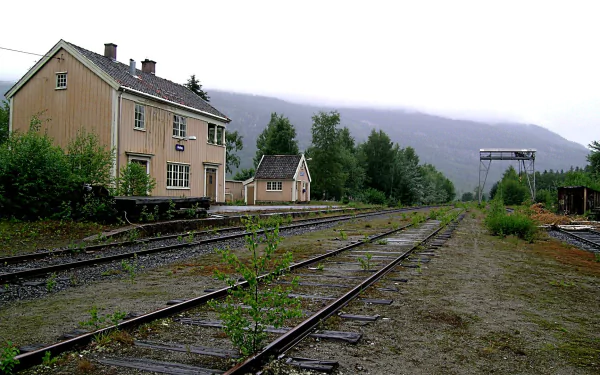 HD image of an old, rustic train station with abandoned tracks, surrounded by lush greenery and misty mountains, used as a desktop wallpaper and background.