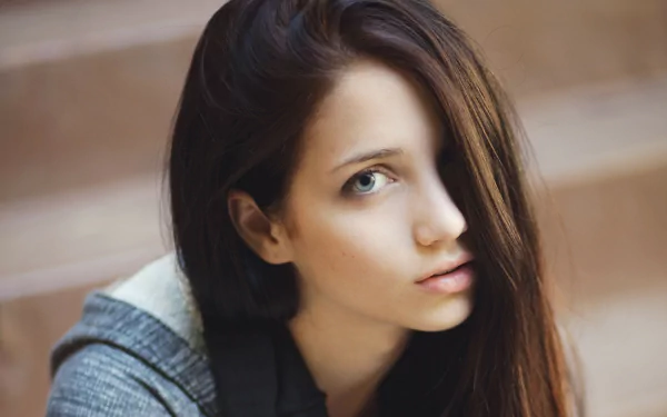 HD desktop wallpaper featuring a close-up portrait of a woman with long brown hair and a thoughtful expression, sitting on steps.