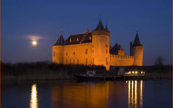 A stunning view of Muiderslot castle illuminated at night, reflected in the calm waters, under a glowing moon. This HD image makes an impressive desktop wallpaper.