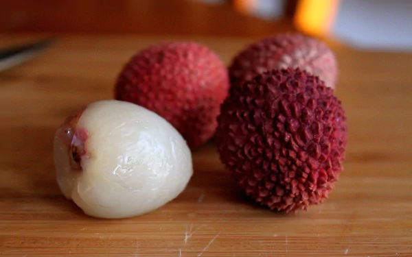Food-themed HD PC desktop wallpaper and background: close-up of lychees on a wooden board — three red-skinned fruits and one peeled white lychee.