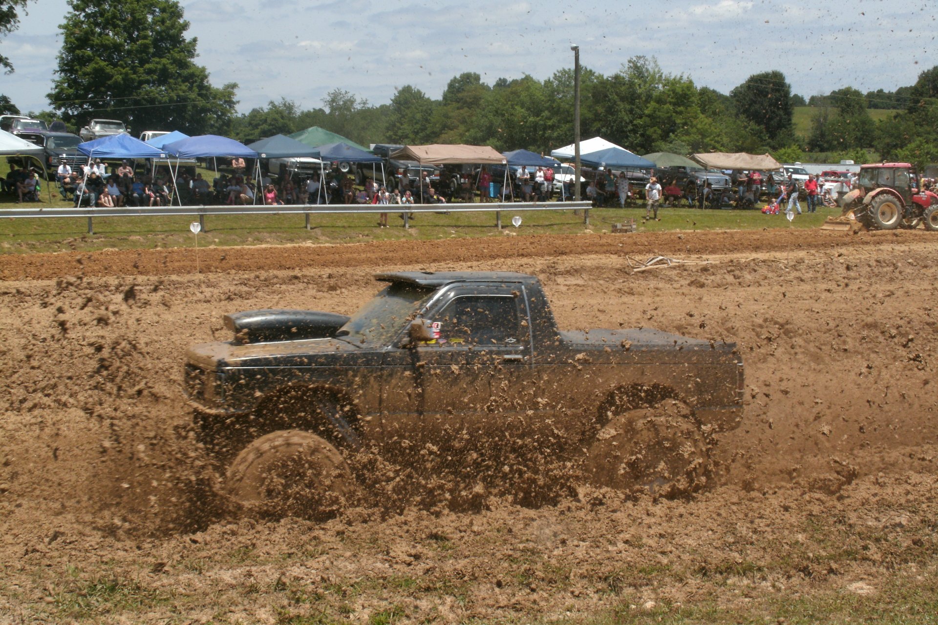A Ford Ranger splashes through muddy terrain at an outdoor event, capturing the excitement of off-road driving amid a lively crowd in the background. 4K Ultra HD quality.