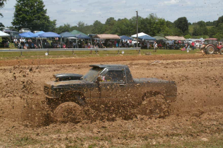A Ford Ranger splashes through muddy terrain at an outdoor event, capturing the excitement of off-road driving amid a lively crowd in the background. 4K Ultra HD quality.